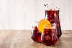 two glasses filled with liquid sitting on top of a wooden table next to an orange slice