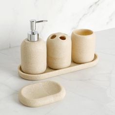 three soap dispensers on a white marble countertop next to a toilet brush holder