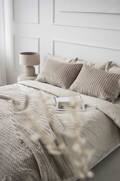 a bed with white sheets and pillows in a bedroom next to a lamp on a table