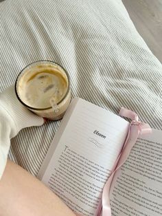 a person laying on a bed reading a book with a cup of coffee next to it