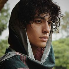 a young man with curly hair wearing a hoodie and looking off to the side