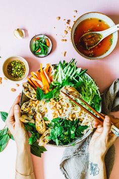 two hands holding chopsticks over a bowl of food on a pink tablecloth