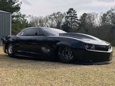 a black sports car parked in front of a metal structure with trees and grass behind it