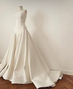 a white wedding dress is on display in front of a wall and wooden flooring