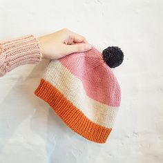 a hand is holding a knitted hat with a pom - pom