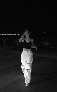 a woman is walking in the dark with her hand on her head and wearing white pants