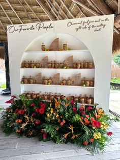 an outdoor display with flowers and spices on it's shelves in front of a thatched roof