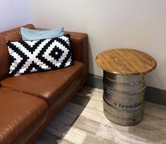 a brown leather couch sitting next to a wooden table with a black and white pillow on it