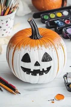 a painted pumpkin sitting on top of a table next to some paint and pencils