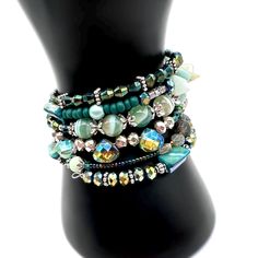 This bohemian gemstone bracelet is just dreamy! It is made on 6 rows of silver memory wire and has iridescence like vibrant peacock feathers. It is made with glass beads, sparkling crystals of all shapes and sizes, silver beads and bead caps, mother of pearl, turquoise gemstones, Labradorite, Aquamarine, in gorgeous green hues and is finished with a large handmade crystal drop.  ★ Return to my main shop page here for more inventory ★ www.etsy.com/shop/bridgetollbeading ★ Read my FAQ's below and Aquamarine Bracelet, Bohemian Bracelet, Memory Wire Bracelet, Green Hues, Memory Wire Bracelets, Bohemian Bracelets, Boho Bracelet, Bracelet Boho, Bracelet Cuff