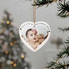 a heart shaped ornament hanging from a tree with a baby's first christmas photo on it