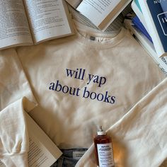 a sweatshirt that says will yap about books next to an open book and a bottle