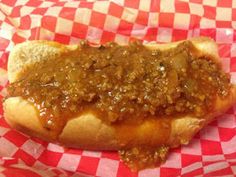 a hot dog covered in chili on top of a red and white checkered paper