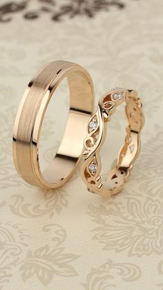 two gold wedding rings with diamond accents on a floral background, one is slightly bent to the side