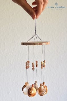 a hand holding a small wooden wind chime with seashells hanging from it