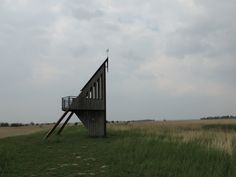 a tall wooden structure sitting on top of a lush green field under a cloudy sky