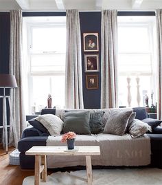 a living room filled with furniture and windows covered in white draping next to a wooden coffee table