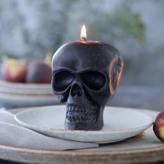 a candle that is on top of a plate with a skull in the middle and an apple next to it