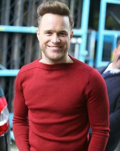 a man in a red sweater is smiling for the camera while another man stands behind him