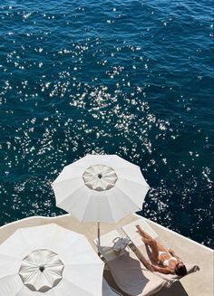 two people lounging on the back of a boat with umbrellas over their heads