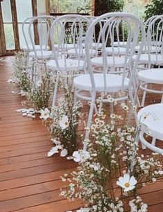 rows of white chairs are lined up on a wooden deck with flowers in the foreground