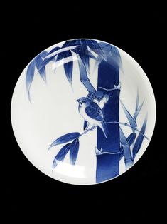 a blue and white plate with a bird sitting on a tree branch in front of it