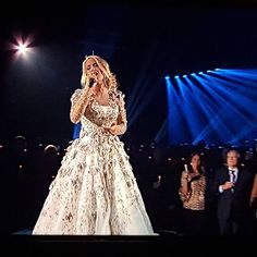 a woman standing on top of a stage wearing a white dress and holding a microphone