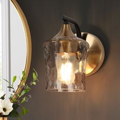 a light that is on the wall next to a vase with some flowers in it