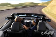 two people in a convertible driving down the road