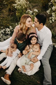 a woman and two men are sitting with their children on the grass in front of flowers