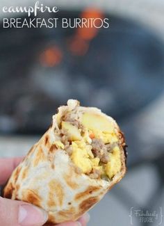 someone is holding up a burrito with eggs and sausage in front of an open fire