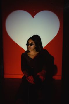 a woman sitting in front of a red heart shaped wall with sunglasses on her face