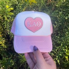 a person holding up a pink and white hat with the word kao on it