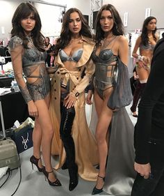 three beautiful women standing next to each other in front of a mirror at a fashion show