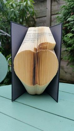 an open book sitting on top of a table next to some plants and trees in the background