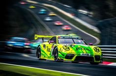 a yellow race car driving on a track with other cars behind it in the background