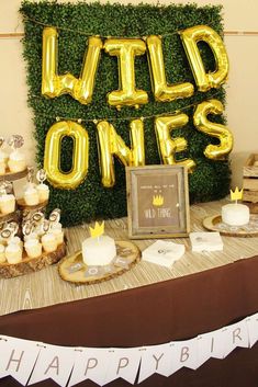 a table topped with cake and cupcakes covered in gold foil letters that spell wild ones