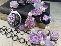 This 28 inch beaded lariat necklace  with a 6 inch pendant featuring some of my own resin art pendants. The main pendant has vintage lavendar enameled chrysanthemum and  dream charm embedded in the resin. Another charm has a resin rose caboschon. There are fresh water pearls, amethyst chrystal beads and mother of pearl coins with a floral print. I also added to the assemblage vintage bakelite roses and an enamaled pink rose caboschon from a vintage pin. The last picture is other similar style pendants in my shop sold separately. Artisan Silver Lariat Necklace For Gift, Silver Artisan Lariat Necklace For Gift, Handmade Purple Lariat Necklace, One Of A Kind Adjustable Wearable Art Jewelry, Pink Wearable Art Jewelry As Gift, Pink Wearable Art Jewelry For Gift, One Of A Kind Artisan Purple Jewelry, Adjustable Czech Glass Artistic Jewelry, Artisan Purple Bracelet Jewelry