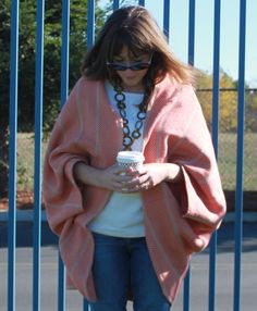 a woman standing in front of a blue fence holding a coffee cup and looking at her cell phone