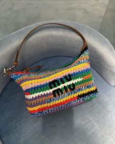 a multicolored purse sitting on top of a gray chair next to a blue cushion