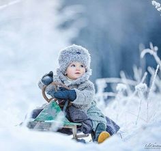 a small child sitting in the snow with a sled