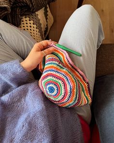 a woman is sitting on the couch with her hand holding a crocheted purse