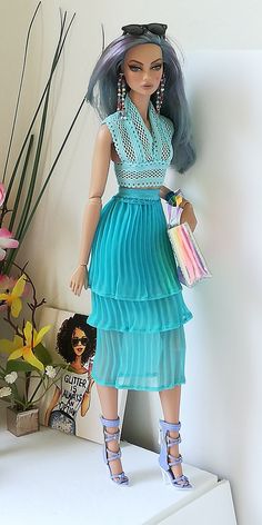 a doll is dressed in a blue dress and holding a purse, standing on a shelf