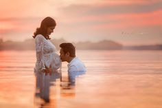 a man and woman are standing in the water at sunset, with their arms around each other