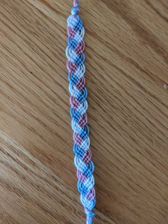 a blue, pink and white braided cord on a wooden table with an object in the background