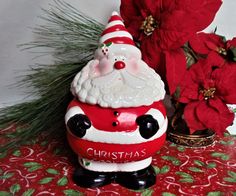 a ceramic santa clause sitting on top of a table next to poinsettis