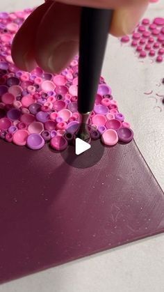 a person is using a pen to paint pink and purple dots on a piece of paper