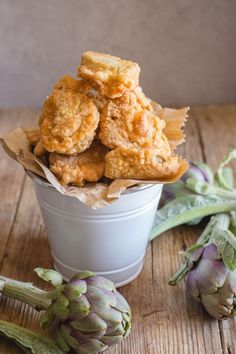 some fried food is in a bowl on a table next to artichokes