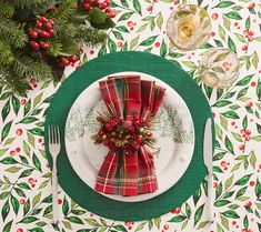 a place setting for christmas dinner with holly napkins and red berries on the table