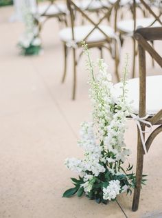 white flowers and greenery sit on the ground in front of rows of wooden chairs